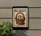 a sign that reads "Egg Basket" with a basket of eggs depicted on it. The sign is mounted on a wall, and there is a plant to the left of the sign.