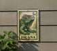 A green and white postage stamp featuring an illustration of an iguana, mounted on a wall next to a plant.