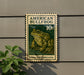 a green and white stamp-like sign with an illustration of a bullfrog, mounted on a wall.