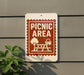 A sign indicating a picnic area is attached to a gray wall, with a plant visible to the left.
