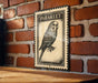 A vintage-style postage stamp featuring a parakeet is displayed on a brick wall.