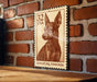 A brown miniature pinscher dog on a wooden surface, with a brick wall in the background.