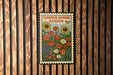 A colorful postage stamp featuring a garden scene with various flowers and plants, displayed on a wooden wall.