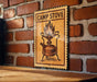 A wooden sign with a picture of a camp stove is mounted on a brick wall.