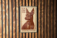A brown and white miniature pinscher dog stamp is displayed on a wooden wall.