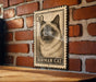 A metal sign featuring a BIRMAN CAT illustration is mounted on a brick wall.