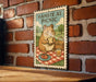 A metal sign with a cartoon hamster sitting on a picnic blanket, eating a sandwich and holding a basket of food, mounted on a brick wall.