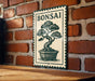 A metal sign with a bonsai tree illustration is mounted on a brick wall.