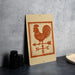 a wooden sign with a rooster and a weather vane, placed on a table next to some black containers.