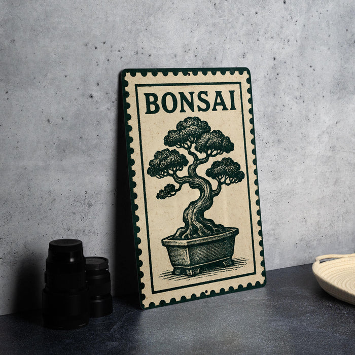 a bonsai tree illustration on a green and white frame, placed on a gray countertop next to a stack of black camera lenses.