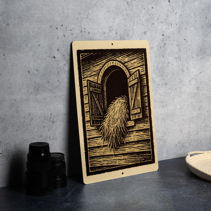 a wooden sign with an illustration of a window and a pile of hay, placed on a table next to some black camera lenses.