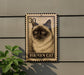 A metal sign featuring a close-up of a Siamese cat's face, mounted on a wall.