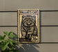 A metal sign with a cat illustration on it, mounted on a wall.