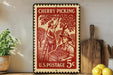 A vintage-style U.S. postage stamp depicting a cherry picking scene, with a woman picking cherries and a man holding a basket of cherries. The stamp is placed on a shelf next to a wooden cutting board and a potted plant.