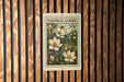 A vintage postage stamp featuring a floral design with white flowers and green leaves, mounted on a wooden wall.