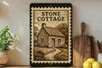 a framed illustration of a stone cottage, with a wooden cutting board and a potted plant to the left.