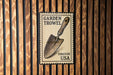 A metal sign with a shovel illustration is mounted on a wooden wall.