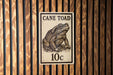 a sign with a drawing of a cane toad, mounted on a wooden wall.