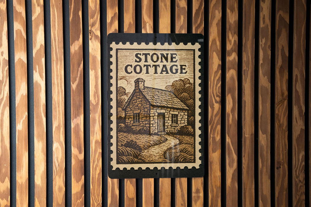 A sign for "Stone Cottage" is displayed on a wooden wall, featuring an illustration of a cottage surrounded by trees and a path leading up to it.