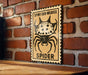 a sign with a spider illustration on it, mounted on a brick wall.