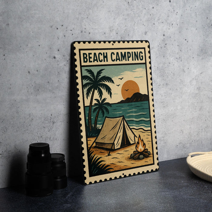 A metal sign with a beach camping scene, featuring a tent, a campfire, palm trees, and a sunset over the ocean.