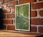 A framed painting depicting a lush forest scene with a winding path through the trees and bluebells growing in the foreground.