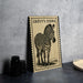 A framed illustration of a zebra is displayed on a table, with a stack of black camera lenses and a woven basket nearby.
