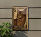 A wooden sign featuring a cat image, mounted on a wall next to a plant.
