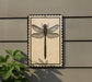 a decorative tile with a detailed illustration of a dragonfly on it, mounted on a wall.