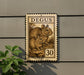 a decorative metal plaque with a stamp-like design, mounted on a wall next to a plant.