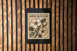 a wooden wall with a black and white stamp-like design depicting an apple blossom on a branch.