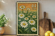 a framed print of a field of white daisies with a green border, placed on a shelf next to a wooden cutting board and some lemons.