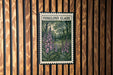 A framed image of purple flowers is displayed on a wooden wall.