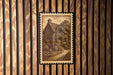 a wooden wall with a framed illustration of a house, which appears to be a cottage or a small building.