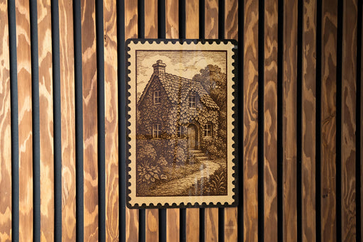 a wooden wall with a framed illustration of a house, which appears to be a cottage or a small building.