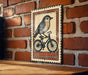 a vintage-style metal sign with a bird riding a bicycle, mounted on a brick wall.