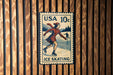 A vintage USA 10c postage stamp featuring an illustration of a woman ice skating, with a wooden background.