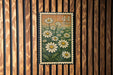 A framed image of a postage stamp with a field of white daisies and the number 44 printed on it, hanging on a wooden wall.