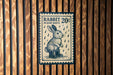 A blue and white postage stamp featuring a rabbit wearing rain boots, with the text "RABBIT 20¢ IN RAIN BOOTS" printed on it.