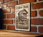 a wooden sign with a black and white illustration of a wooden house on a brick wall.