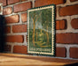 A metal sign with a green border and a painting of trees hangs on a brick wall.