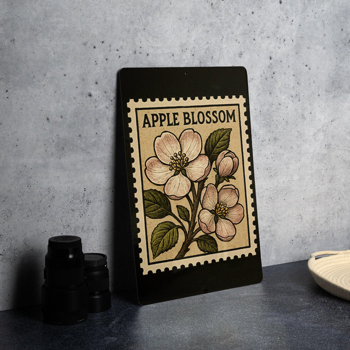 a framed print of an apple blossom on a black background, placed on a countertop next to some black camera lenses.