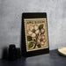 a framed print of an apple blossom on a black background, placed on a countertop next to some black camera lenses.