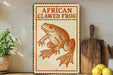 a sign with an illustration of an African clawed frog, placed on a wooden surface next to a wooden cutting board and some lemons.