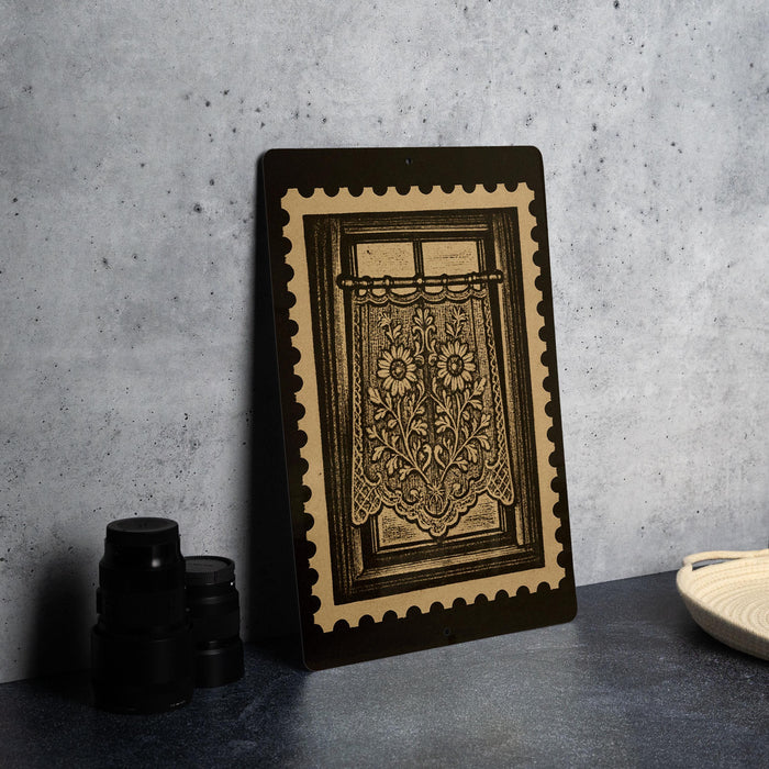 a framed artwork depicting a window with a floral design, placed on a dark surface next to a stack of black camera lenses.