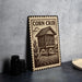 a wooden sign with a house illustration, placed on a table next to some black camera lenses.