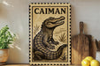 a framed illustration of a crocodile, with a wooden cutting board and a potted plant in the background.