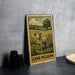 A metal sign with a pastoral scene depicting a lamb in a grassy field, with a tree and flowers in the background.