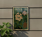 A framed poster with a floral design hangs on a wall, featuring a collection of flowers and leaves.