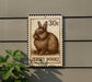 A metal sign featuring a rabbit on a postage stamp, mounted on a wall.
